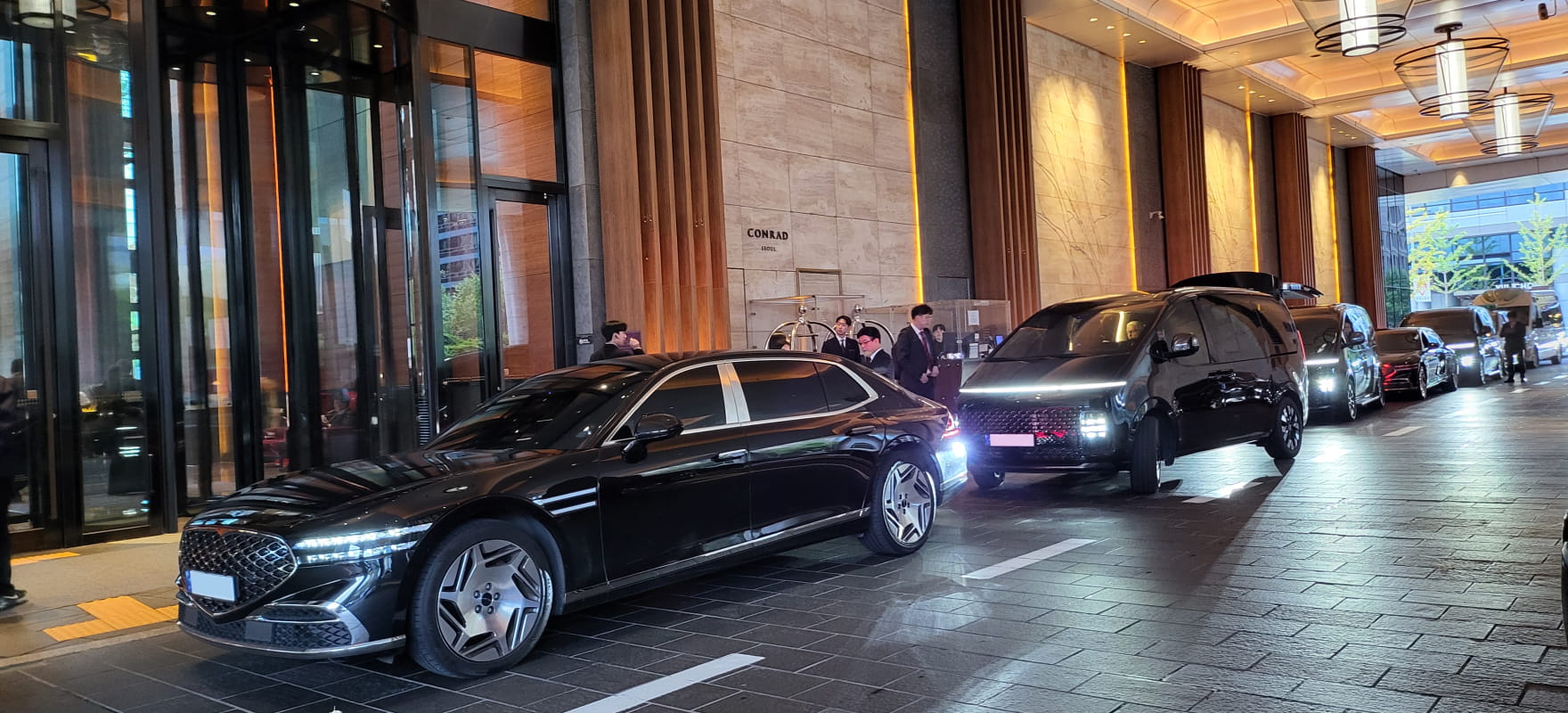 A lineup of black premium protocol vehicles, including Genesis G90 and Staria, at the Conrad Seoul hotel entrance for the AFC event.