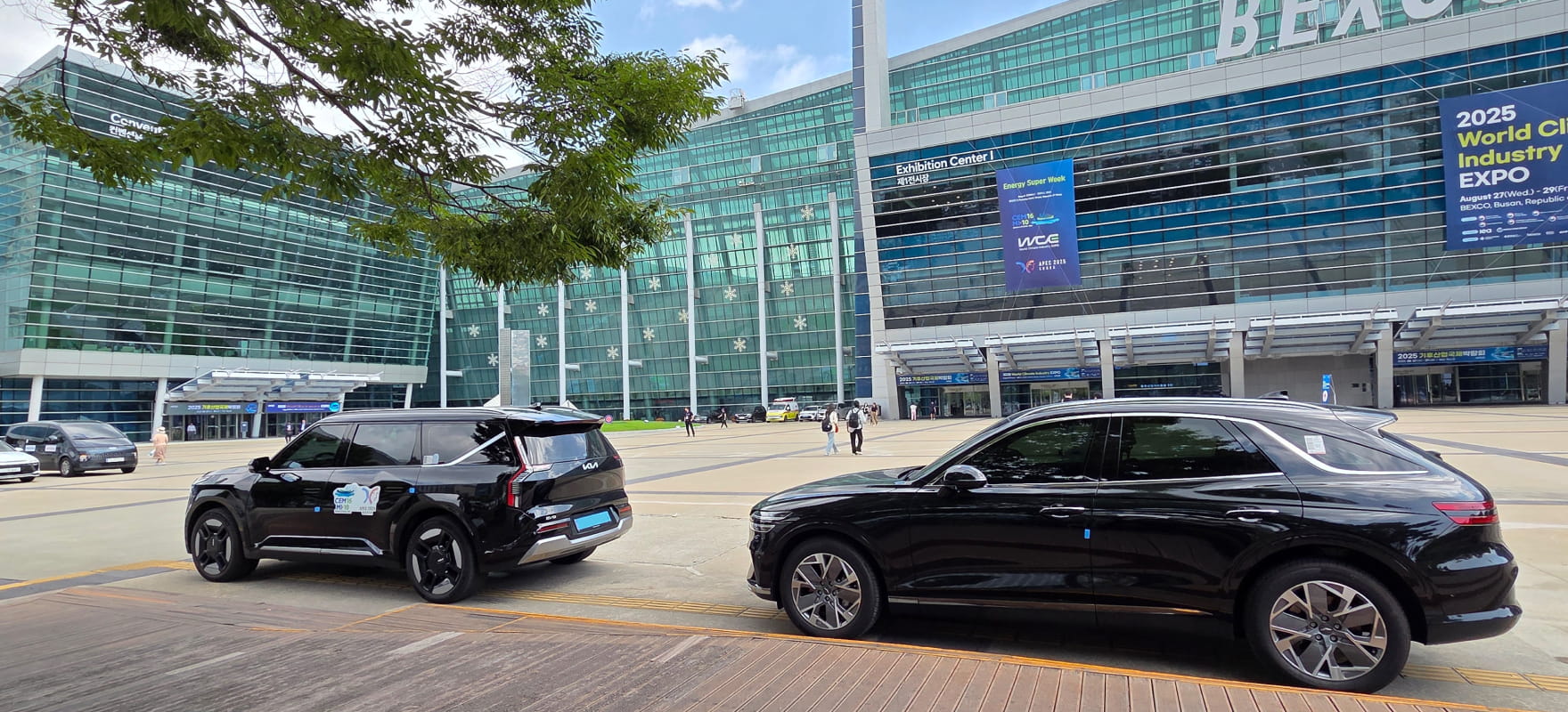 Black Kia EV9 and Genesis GV80 premium vehicles stationed at BEXCO Exhibition Center 1 for APEC summit shuttle services.